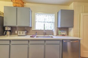 A kitchen with grey cabinets, a stainless steel refrigerator, a coffee maker, a toaster, and a window with a view of trees. - Lovely 4BR Lakeview - Game Room - Foosball (Seattle)