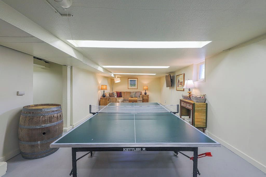Une table de ping-pong dans une pièce où se trouvent un canapé, un tonneau en bois et une armoire avec une lampe.