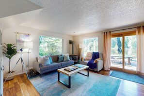 A spacious living room with a sofa, coffee table, and a large window offering a view of the outdoors. - 3BR waterfront home with gas grill and deck (Lacey)