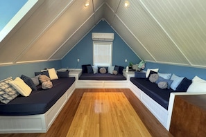 Ein Schlafzimmer im Loft-Stil mit schrägem Dach, integrierten Sitzbereichen und einem zentralen Fenster.