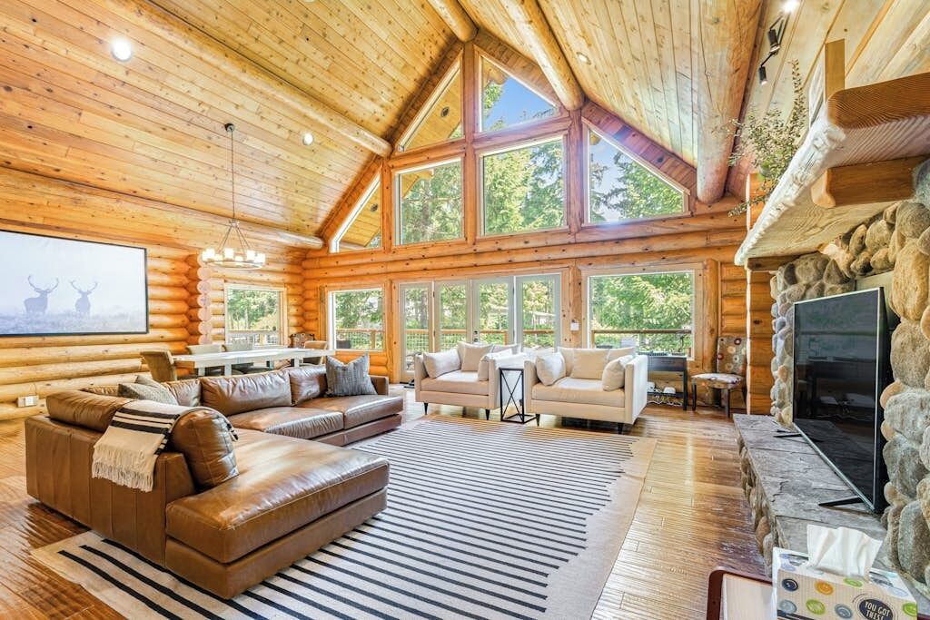 A log cabin interior with a fireplace, a large window, and a sofa.