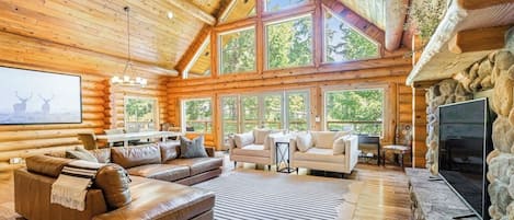 A log cabin interior with a fireplace, a large window, and a sofa.