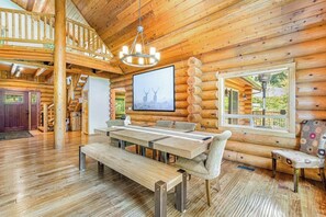 A log cabin interior with a dining area, wooden floors, a chandelier, and a large window. - Custom 3BR Golf Course View - Chef's Kitchen (Union)