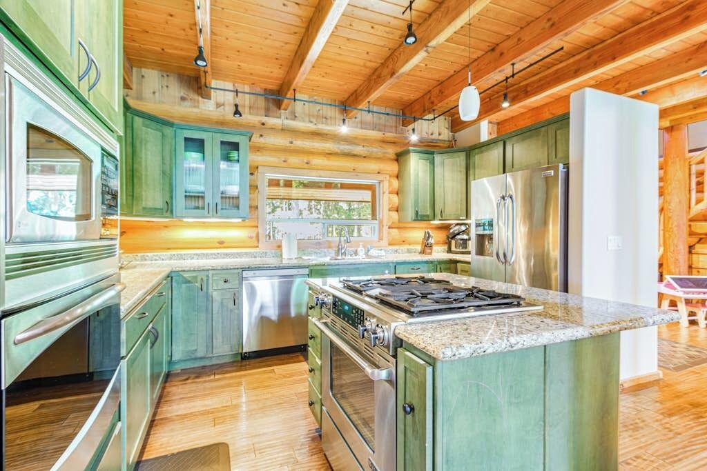 A log cabin kitchen with wooden cabinets, a stainless steel refrigerator, and a granite countertop.