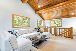 A living room with a wooden ceiling, a white sofa, a coffee table, and a view of the outdoors through large windows. - Custom 3BR Golf Course View - Chef's Kitchen (Union)