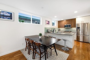 A modern kitchen with a dining area, wooden cabinets, stainless steel appliances, and a view of a mountain through a window. - Corner 3BR - Balcony - Street Parking - Washer Dryer (Seattle)