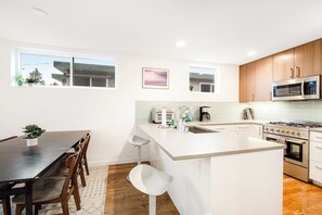 A modern kitchen with a central island, wooden cabinets, a stainless steel microwave, and a dining area with a table and chairs. - Corner 3BR - Balcony - Street Parking - Washer Dryer (Seattle)