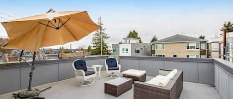 Una terraza en la azotea con mobiliario exterior, un amplio paraguas y vistas de edificios circundantes.