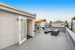 Un espace extérieur aménagé en terrasse, avec une porte-fenêtre donnant accès à l’intérieur, des sièges et une vue sur les bâtiments voisins.