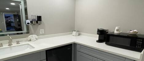 Une salle de bain moderne avec un lavabo, un miroir, un distributeur de savon et une machine à café posée sur le comptoir.