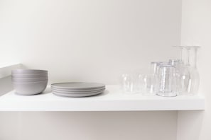 A white shelf with stacked bowls, plates, and clear glassware.
