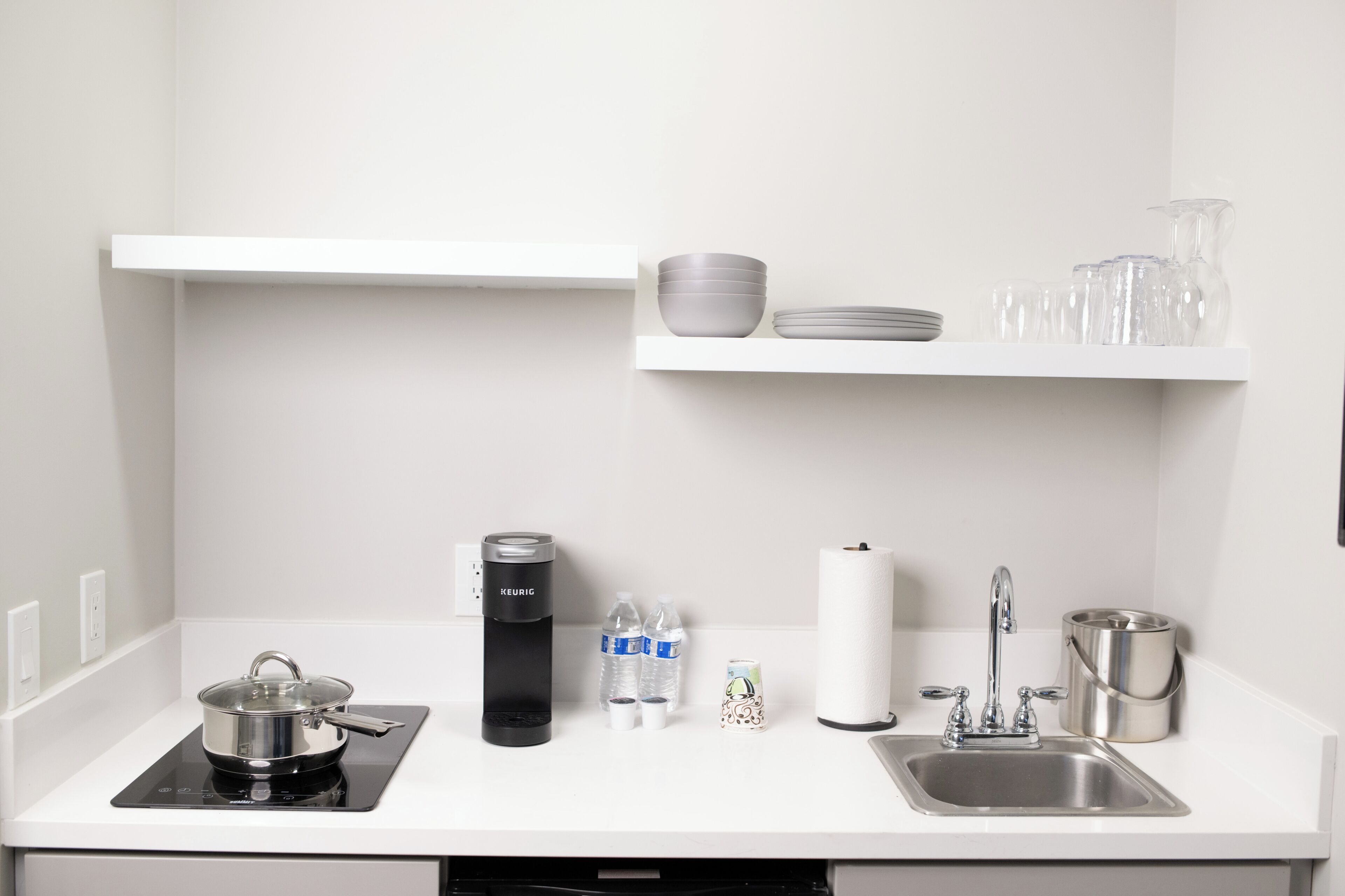 A kitchen with a stove, kettle, sink, and shelves with dishes and glasses.
