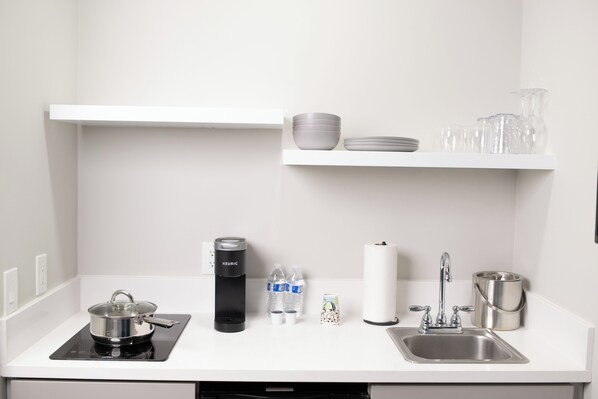 A kitchen with a stove, kettle, sink, and shelves with dishes and glasses.