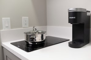 A kitchen with a black induction cooktop, a stainless steel pot, and a black Keurig coffee maker.
