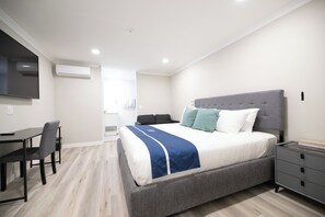 A modern bedroom with a large bed, bedside tables, a desk, and a flat-screen TV.