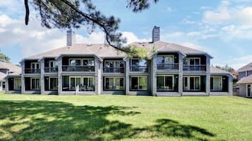Une maison à deux étages avec une grande pelouse à l’avant, de nombreuses fenêtres et un balcon à l’étage supérieur.