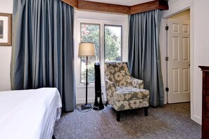 A hotel room with a bed, a chair, a lamp, and a window with curtains.