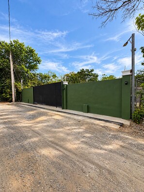 A gated driveway leading to a building with a green exterior wall.