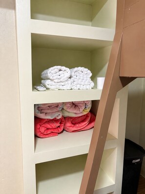 A storage unit with shelves holding folded blankets in white, pink, and red colors.