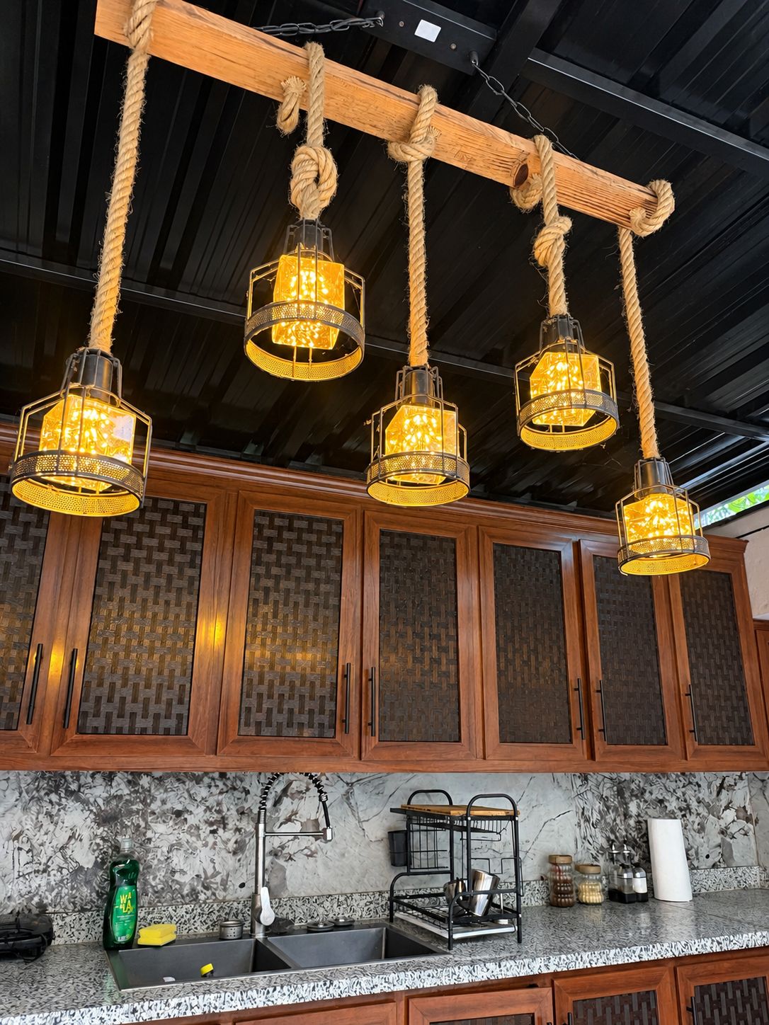 A kitchen with wooden cabinets, a marble countertop, and a hanging light fixture with a rope design.