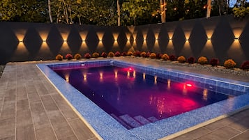 Une piscine rectangulaire dont le bord est recouvert de carreaux, entourée d’un muret doté d’un éclairage intégré.