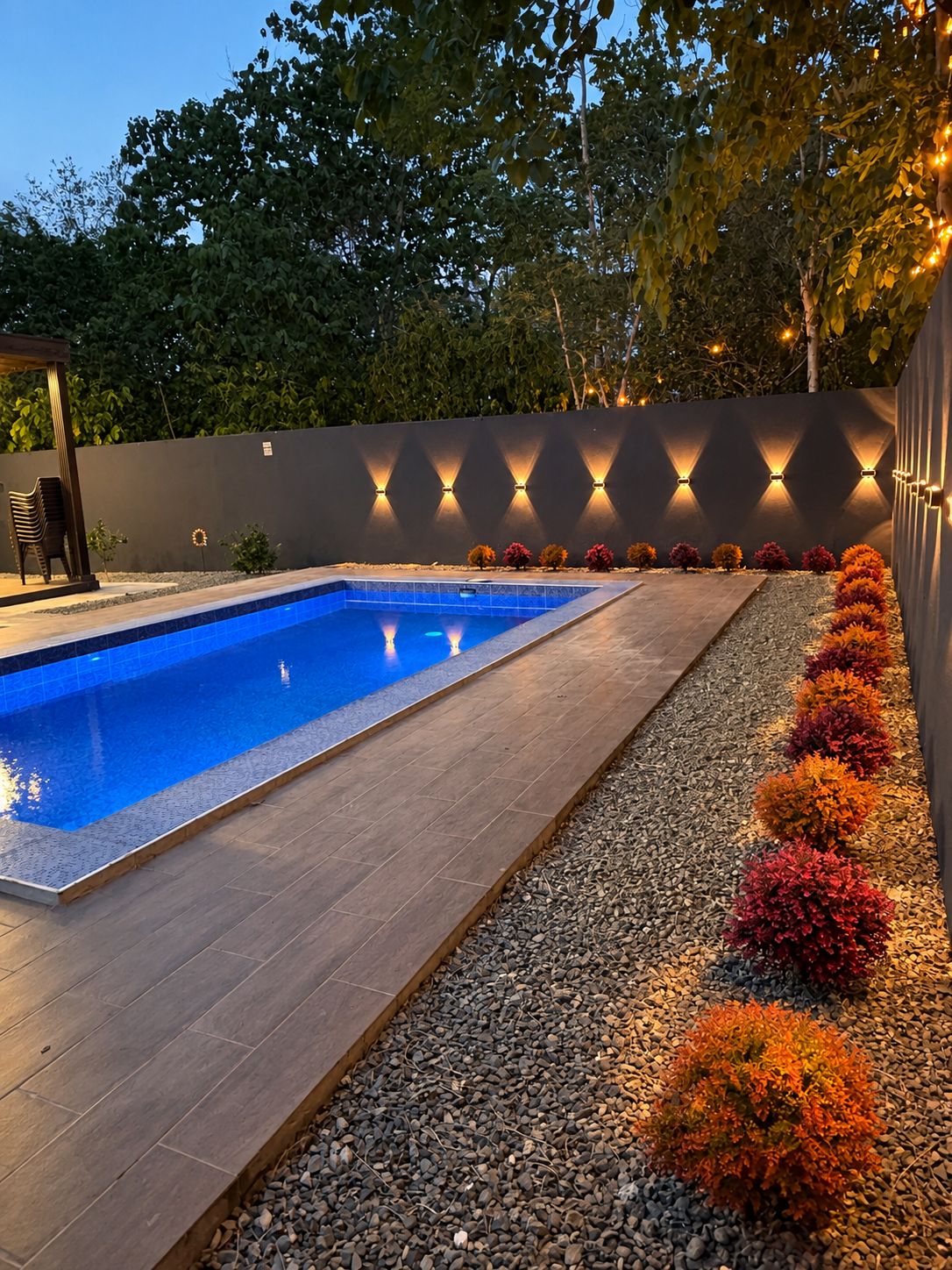 A swimming pool with a tiled deck, surrounded by a low wall with decorative lighting.