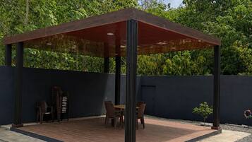 Un área de estar al aire libre con techo, con una mesa y sillas, rodeada por un muro bajo y un suelo de grava.