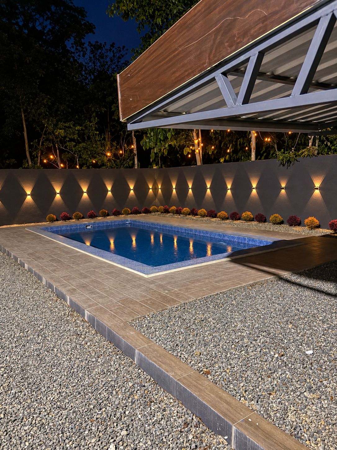 Ein Pool mit Kiesrand, umgeben von einer niedrigen Mauer mit dekorativer Beleuchtung.