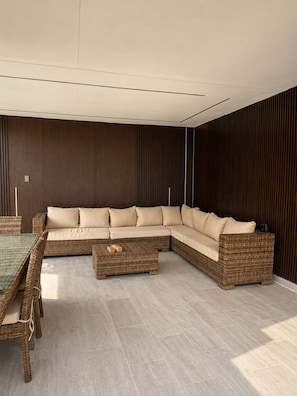 Una sala moderna con un sofá modular, una mesa de centro de vidrio y muebles de mimbre.