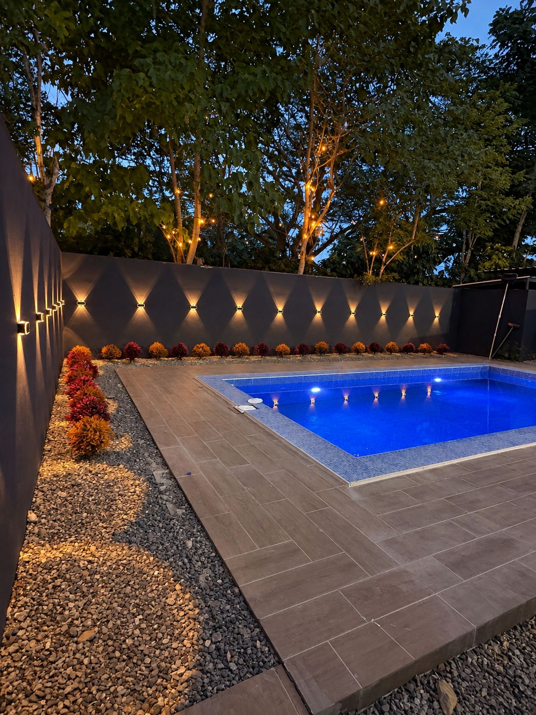 Una piscina con borde de baldosas, rodeada por un muro bajo con iluminación integrada.