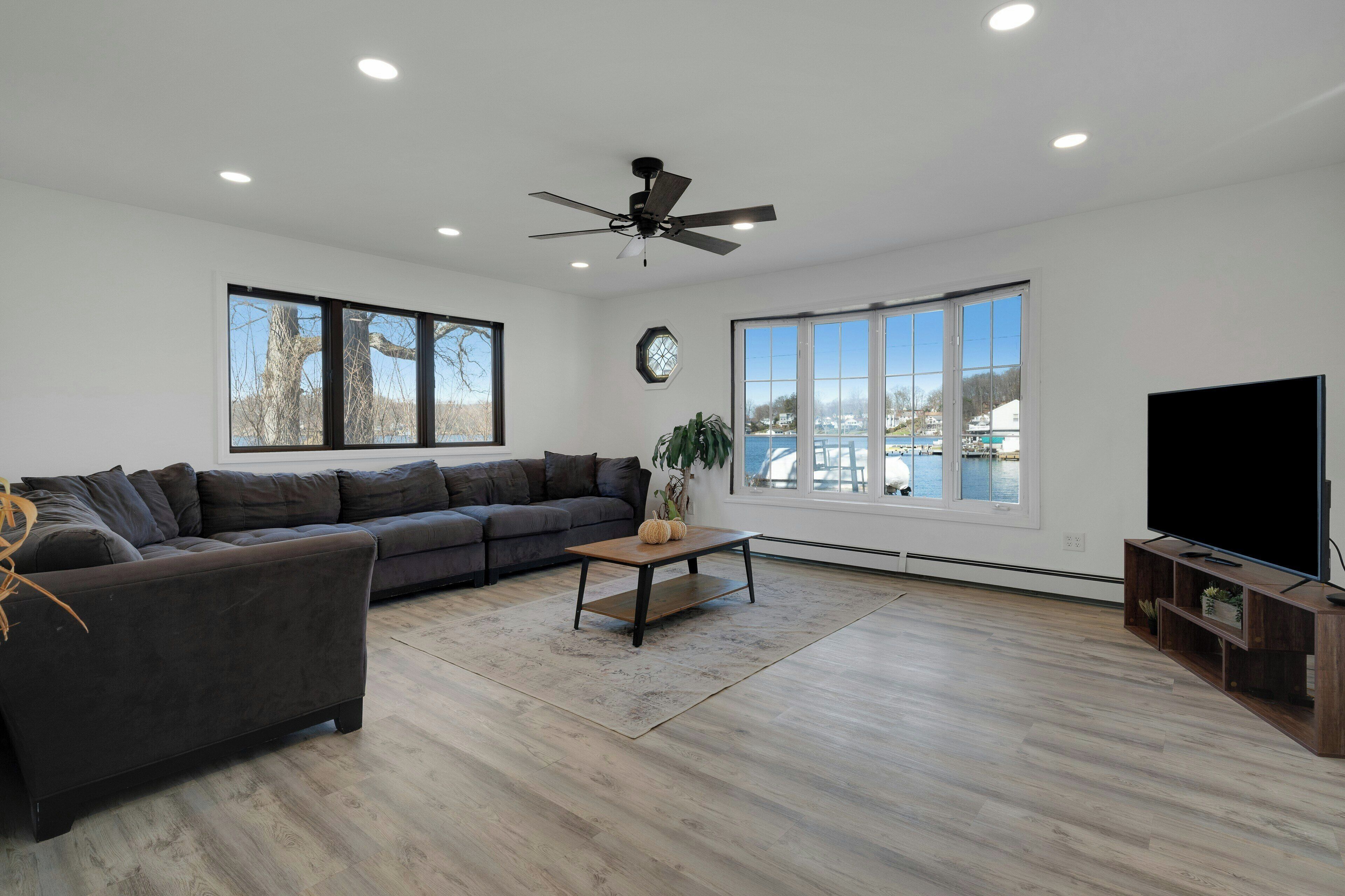 A spacious living room with a dark grey sectional sofa, a wooden coffee table, and a flat-screen TV on a wooden stand.