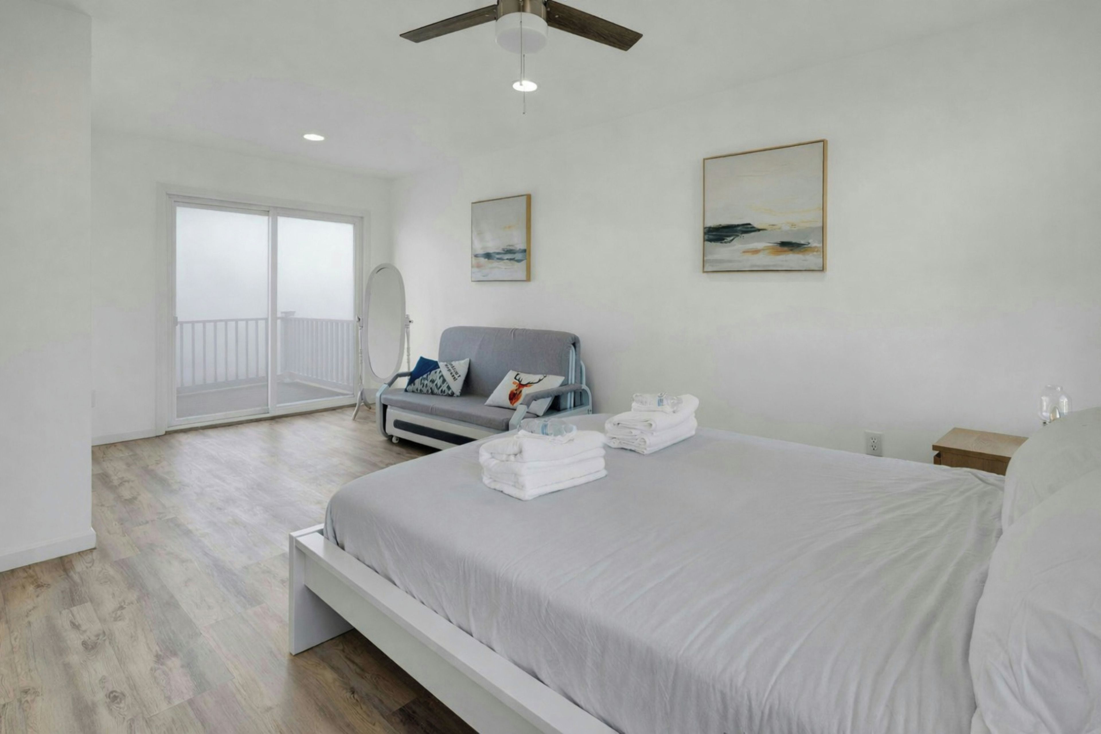 Une chambre moderne avec un grand lit, un canapé gris et un balcon doté d’une balustrade blanche.