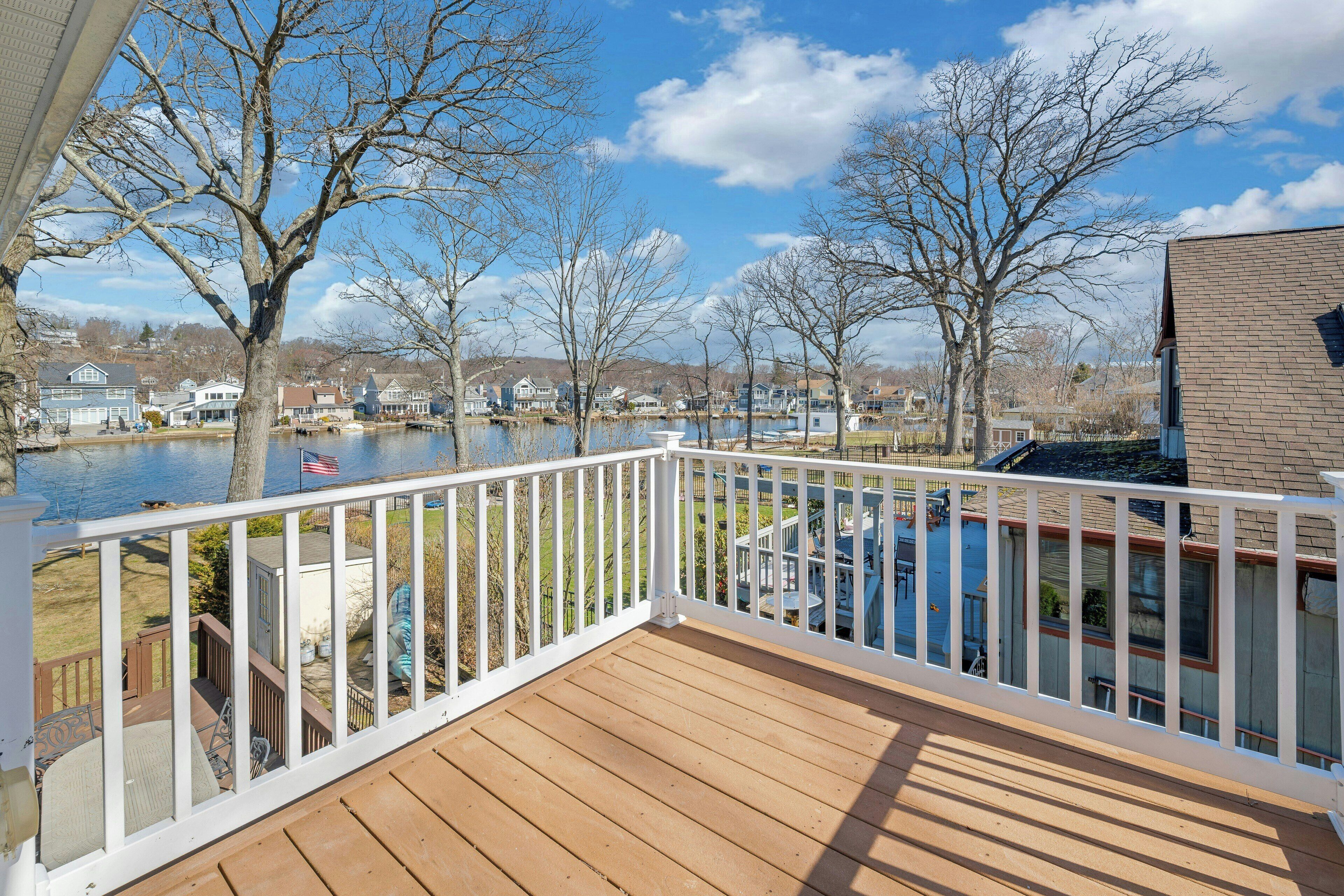A wooden deck with a white railing overlooking a body of water and a residential area.
