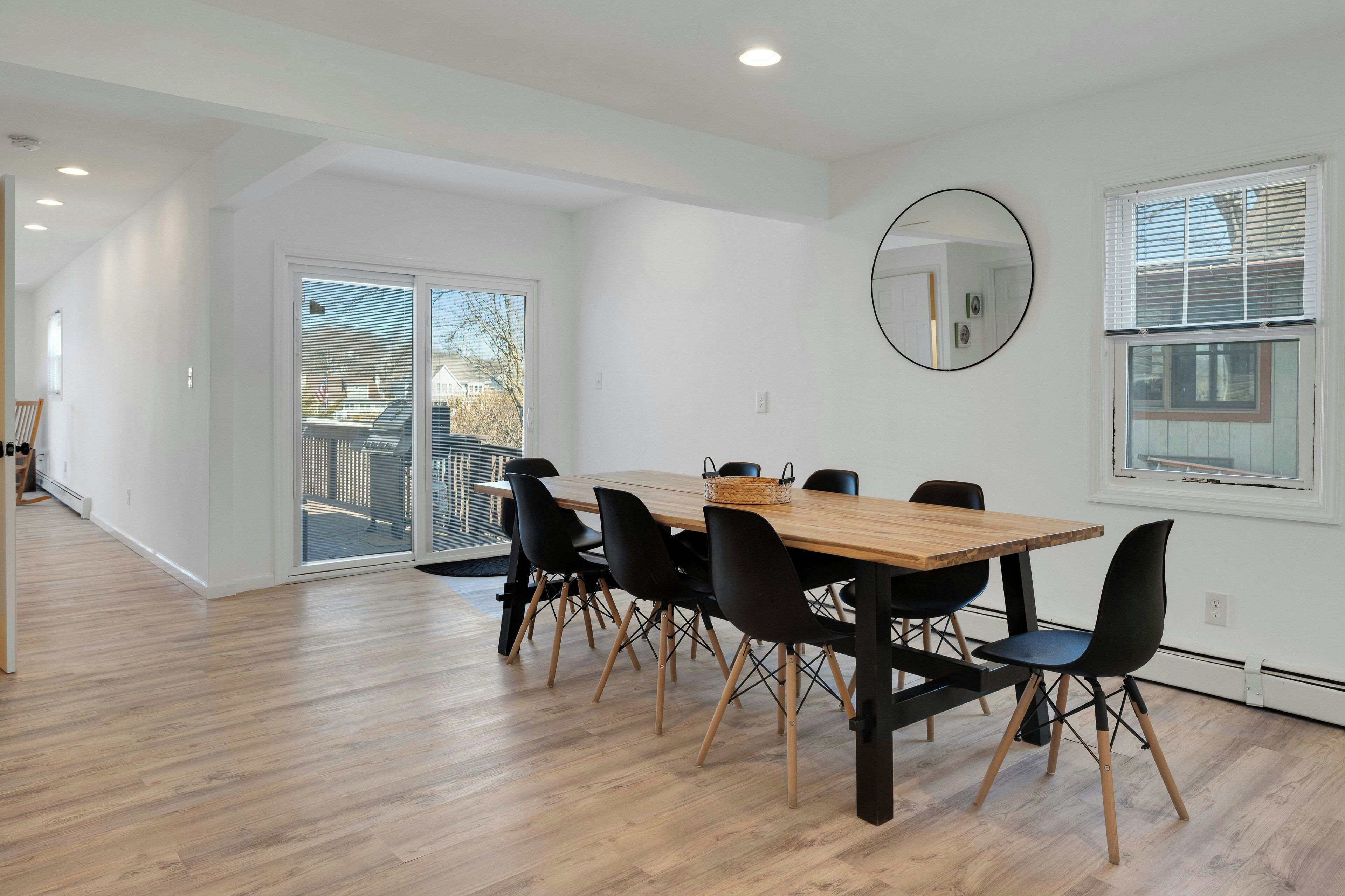 Zona pranzo moderna con tavolo in legno, sedie nere, ampie finestre e una lampada a soffitto.