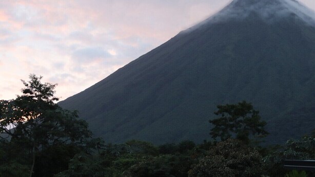 Una montagna con una cima avvolta dalle nuvole, circondata da alberi.
