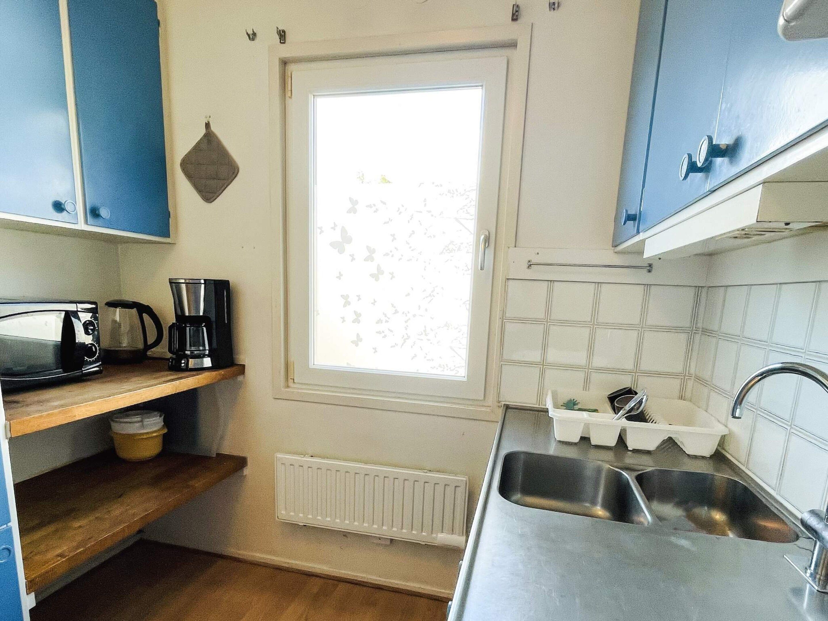 Uma cozinha compacta com micro-ondas, cafeteira e uma janela com padrão de borboleta.