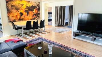 Una sala de estar moderna con un sofá, una mesa de centro, televisor, zona de comedor con sillas y un cuadro abstracto grande en la pared.