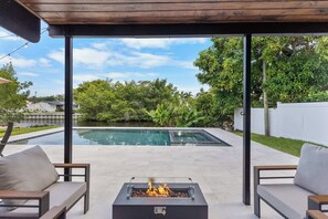 Un patio exterior con piscina, fogata y zona de estar.