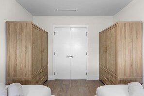 A room with a white door, two wooden wardrobes, and a bed with white bedding. - Waterfront Pool I Paddleboards, Firepit + Fishing (Miami)