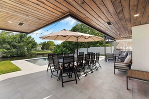 An outdoor patio with a pool, surrounded by greenery, featuring a dining area with chairs and an umbrella. - Waterfront Pool I Paddleboards, Firepit + Fishing (Miami)