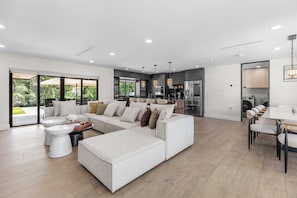Ein modernes Wohnzimmer mit einem Ecksofa, einem Esstisch mit Stühlen und einer Küchenzeile inklusive Kühlschrank und Herd.