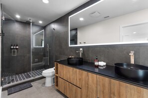 Un baño moderno con un espejo grande, dos lavamanos negros, un inodoro y una zona de ducha.