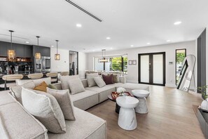 Ein modernes Wohnzimmer mit einer Eckcouch, einem Essbereich mit Bar und einer großen Glasschiebetür, die zu einem Balkon führt.