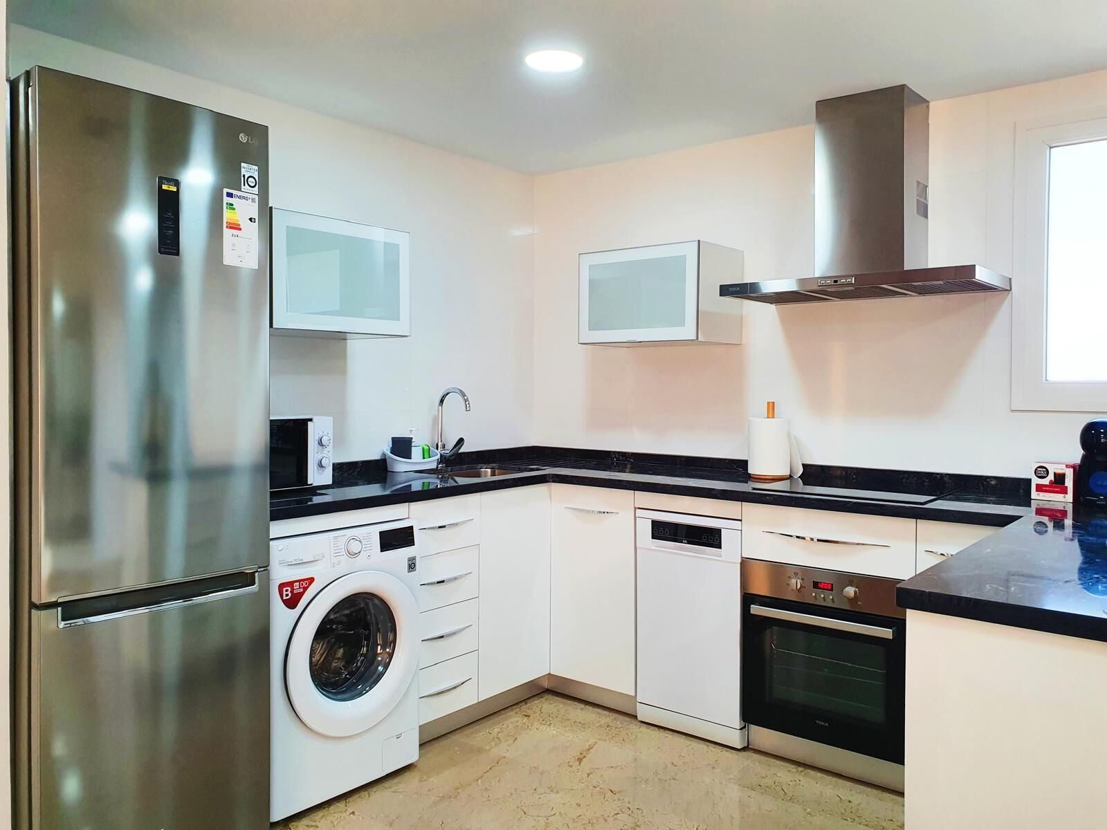 Een moderne keuken met een roestvrijstalen koelkast, een geïntegreerde wasmachine, een magnetron, een vaatwasser en een fornuis.
