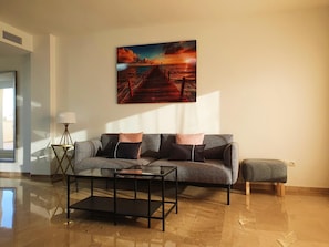 Ein modernes Wohnzimmer mit einer Couch, einem Couchtisch und einem Gemälde von einem Sonnenuntergang über einem Steg.