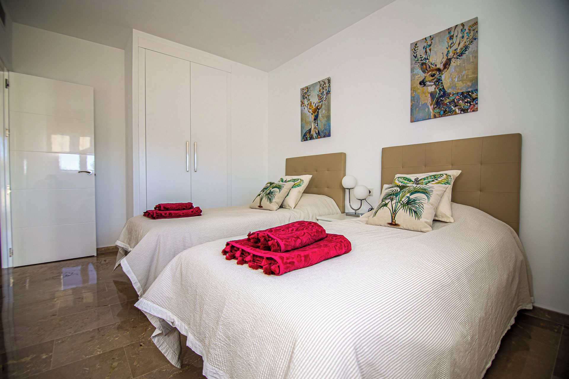 A hotel room with two beds, a wardrobe, and artwork on the walls.