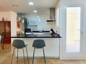 Eine moderne Küche mit schwarzem Arbeitsplatz, zwei Barhocker, einer Mikrowelle und einer Edelstahl-Dunstabzugshaube.