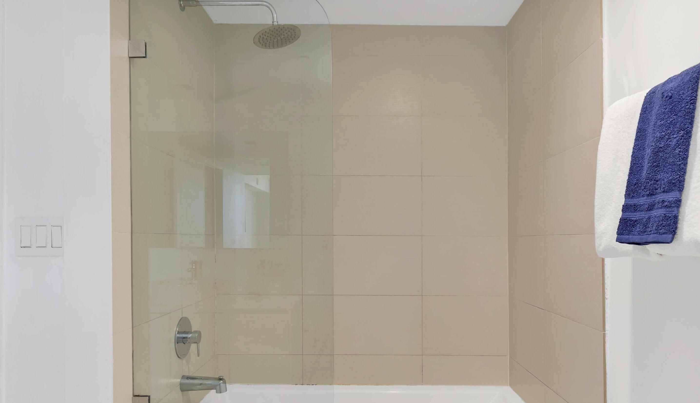 A modern bathroom with a glass-enclosed shower, a white bathtub, and a towel hanging on the wall.