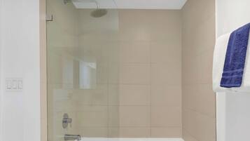 A modern bathroom with a glass-enclosed shower, a white bathtub, and a towel hanging on the wall.