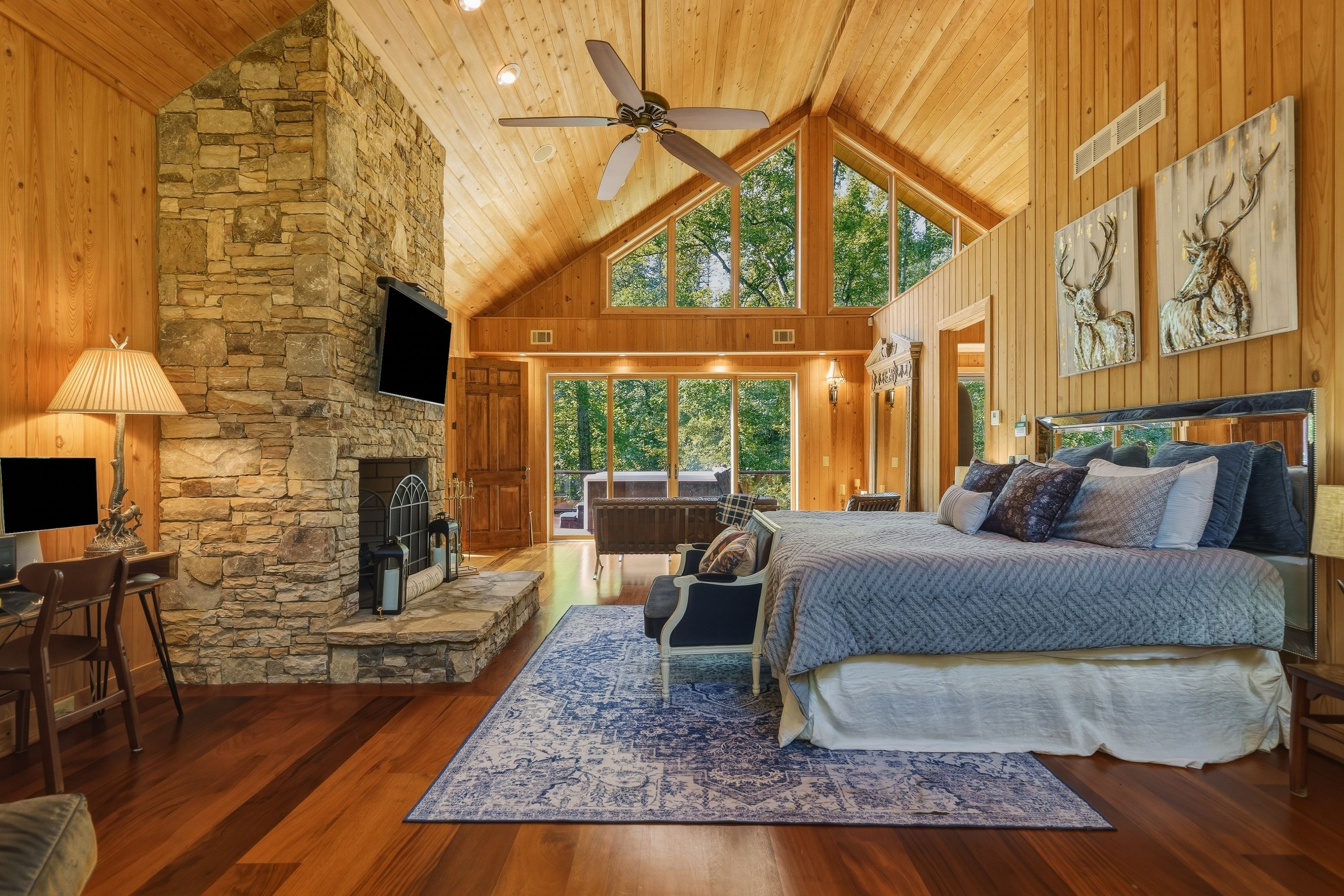 A spacious bedroom with a large bed, a stone fireplace, and a view of the outdoors.
